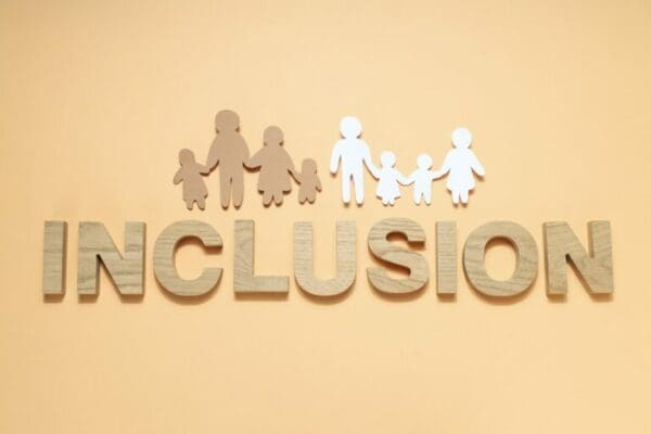 Inclusion spelled with wooden letters below coloured diverse people cutouts