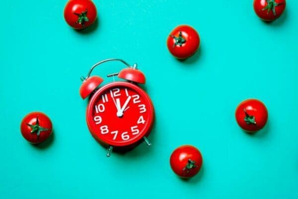 Tomatoes and alarm clock for Pomodoro Technique on blue background