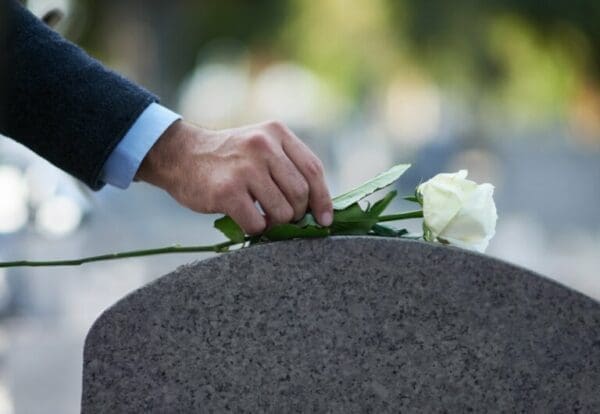 Hand of a man placing a white rose on his dad's grave