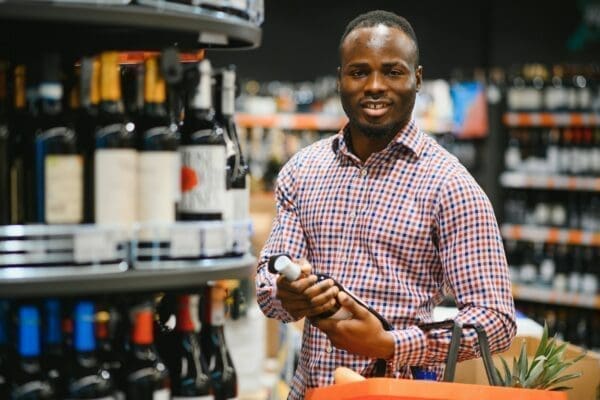 African American man holding bottle of wine and looking at it while standing in a wine store