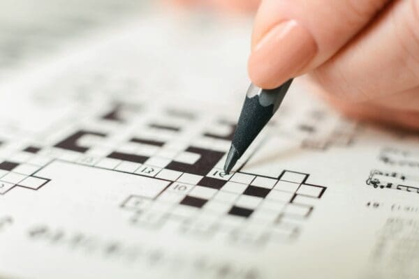 Person Using Pencil to Solve Crossword Puzzle problem solving game