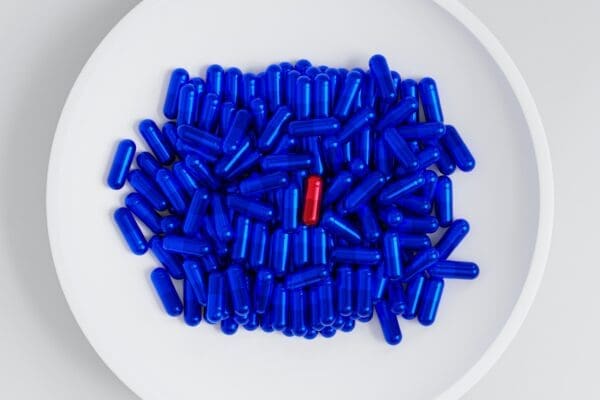 Single red pill among blue pills on a white plate