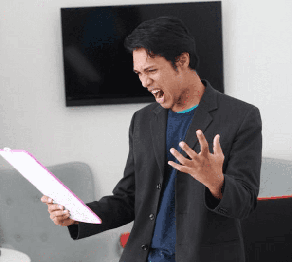 A man shouting in frustration at a piece of paper or board in has right hand