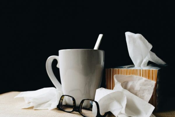 a mug, glasses and several tissues on a table against a dark background