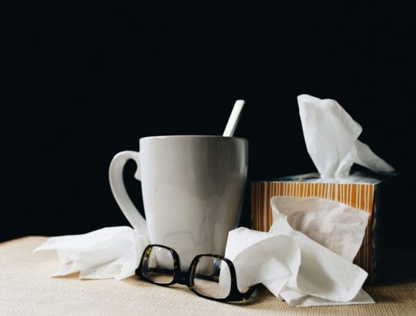 a mug, glasses and several tissues on a table against a dark background cold at work