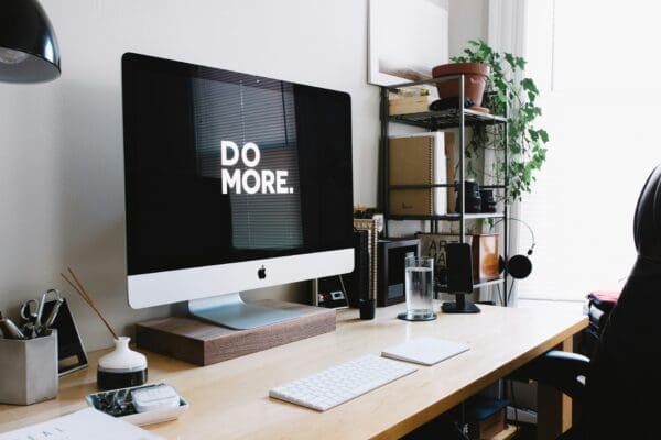 An apple iMac on a desk with a desktop screensaver that says 'Do More' because doing a great job isn't enough
